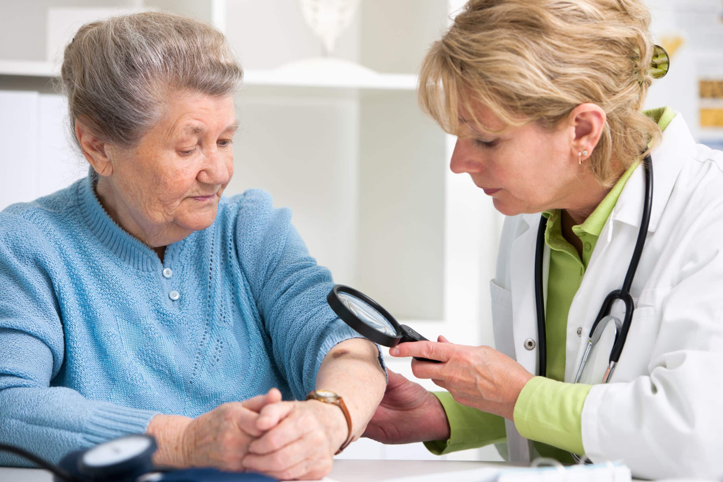 A doctor inspecting an elderly woman’s skin for signs of skin cancer.