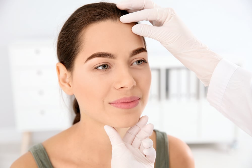Doctor checking a young woman's face for signs of skin cancer.