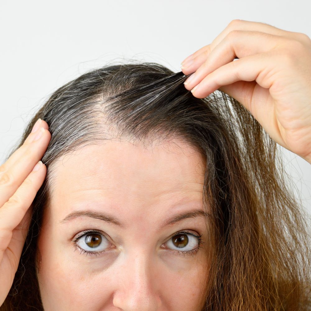 woman is checking white hair while looking at the mirror