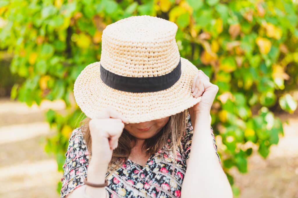 Woman holds a straw hat over her face during the Florida winter to avoid actinic keratosis